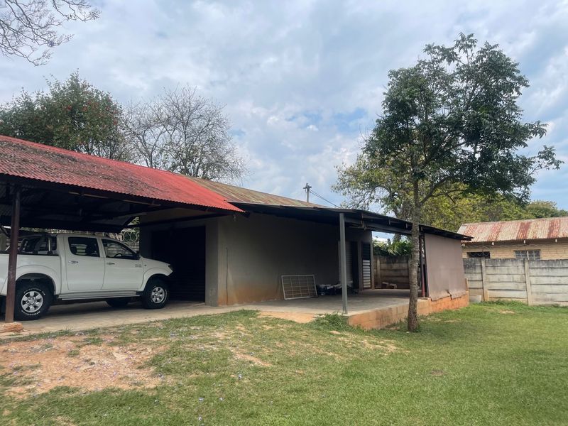 Rear view of the property featuring a large carport structure with a corrugated metal roof and an adjacent open concrete patio area.