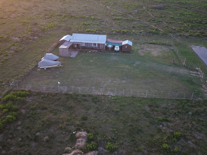 Aerial view of a rural property featuring a main dwelling with a corrugated metal roof, outbuildings, and a fenced yard area.