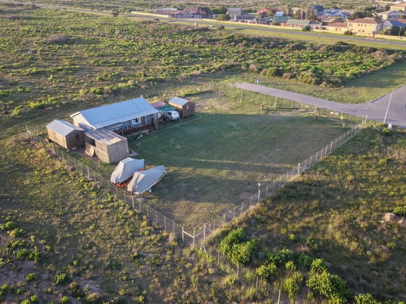Aerial view of a residential property featuring a main dwelling with a metal roof, multiple outbuildings, and a large fenced yard.