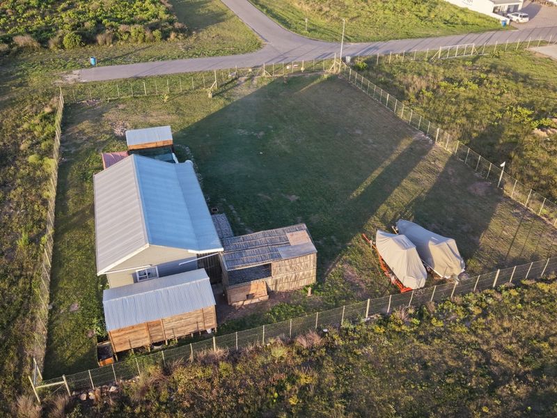 Aerial view of a residential property featuring a metal-roofed dwelling with timber cladding, set within a large, fully fenced plot.