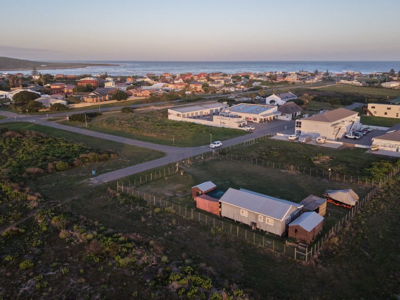 Aerial view of the property showing the main dwelling, outbuildings, fenced yard, and surrounding coastal neighborhood landscape.