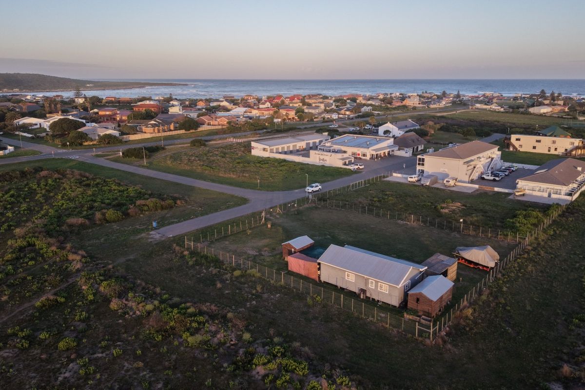 Aerial view of the property showing the main dwelling, outbuildings, fenced yard, and surrounding coastal neighborhood landscape.