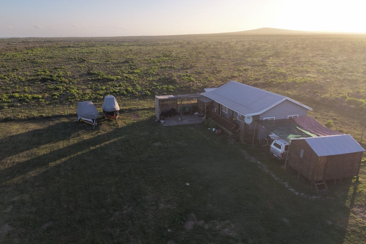 Aerial view of a rural property featuring a main dwelling with a corrugated metal roof, attached patio, and surrounding open land.