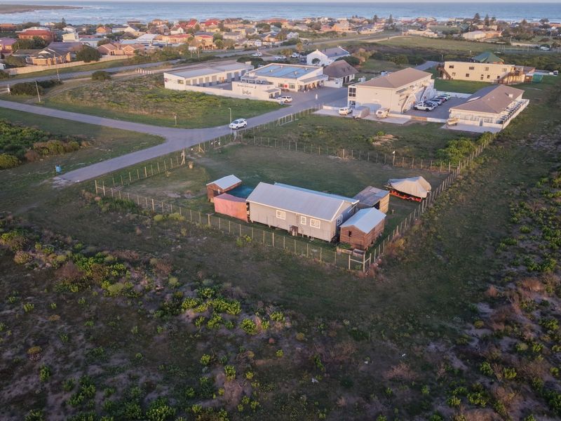 Aerial view of the property showing the main dwelling, outbuildings, and fenced grounds situated in a coastal residential area.