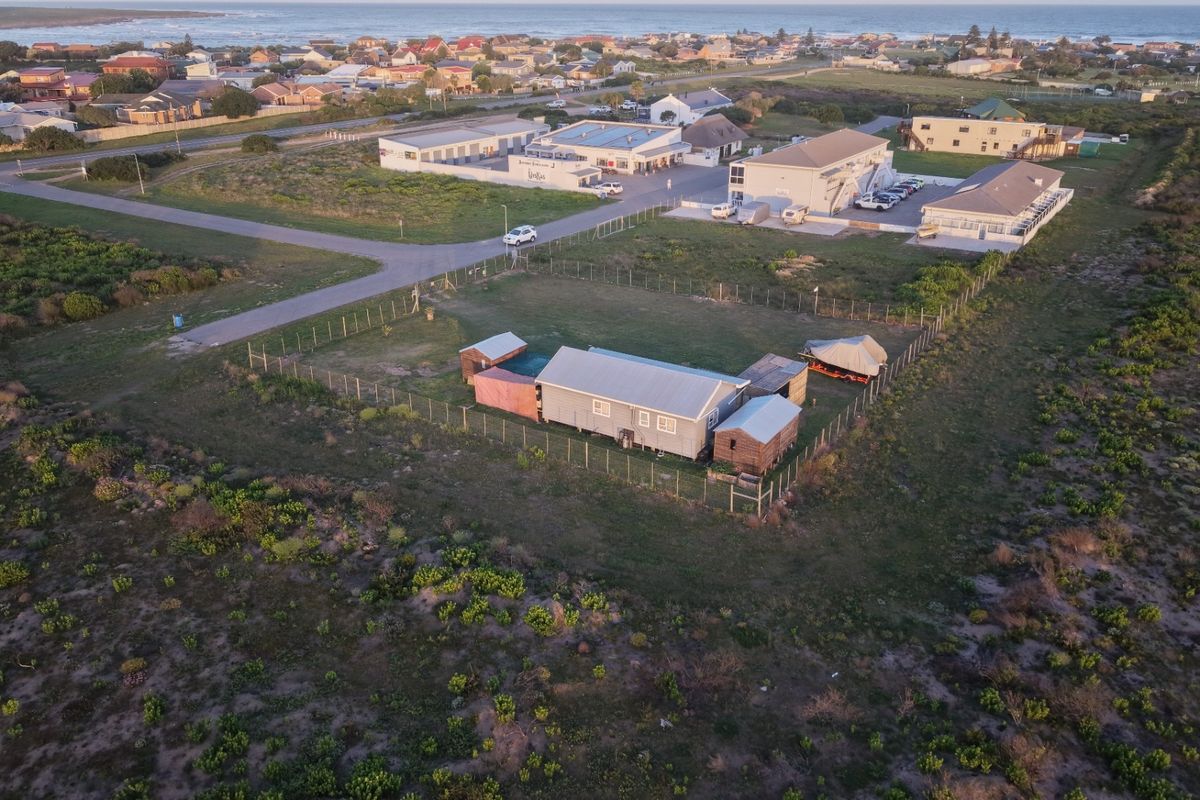 Aerial view of the property showing the main dwelling, outbuildings, and fenced grounds situated in a coastal residential area.