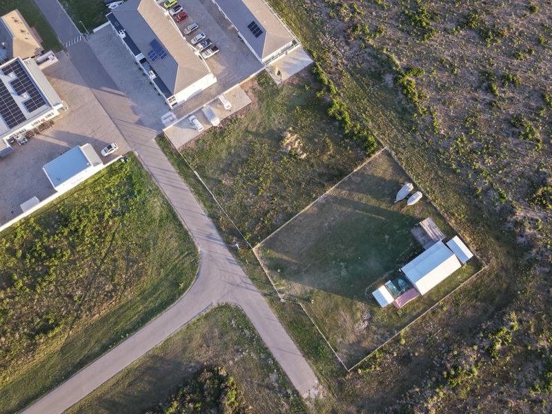 Aerial view of the property showing the main building with solar panels, paved driveway, and a fenced rear yard with an outbuilding.