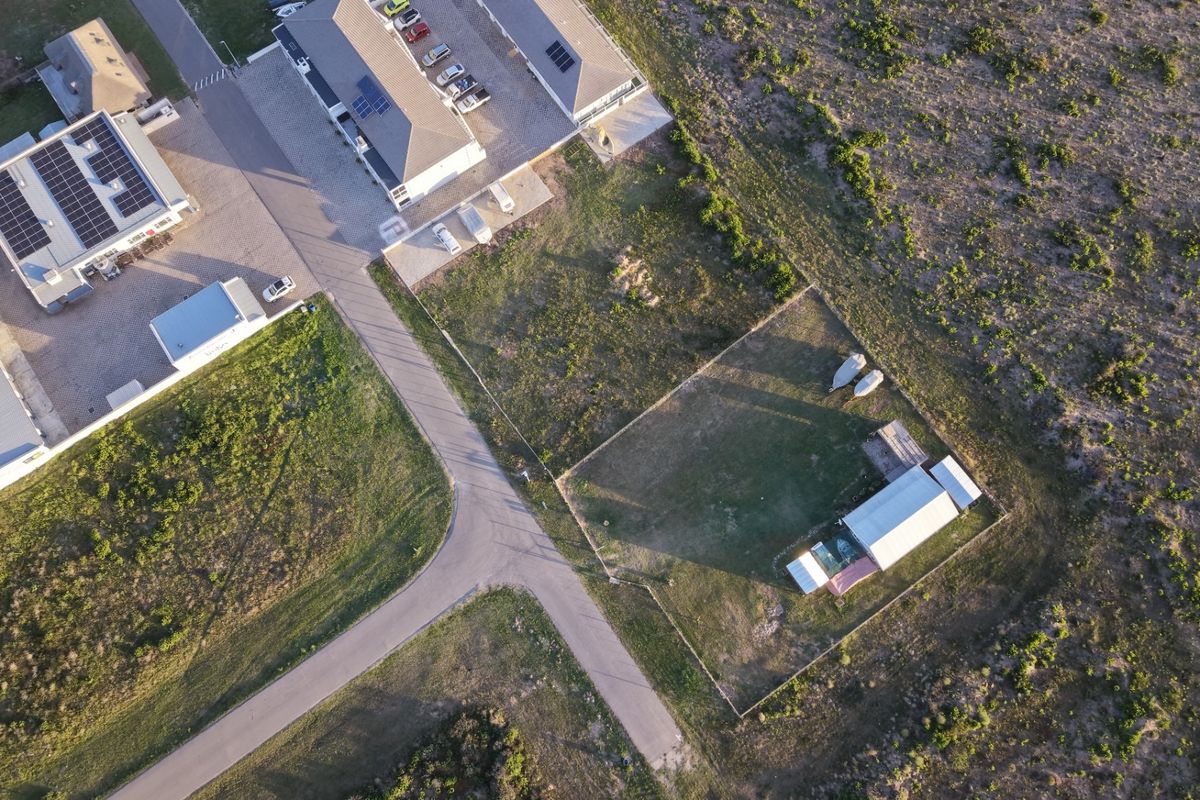 Aerial view of the property showing the main building with solar panels, paved driveway, and a fenced rear yard with an outbuilding.