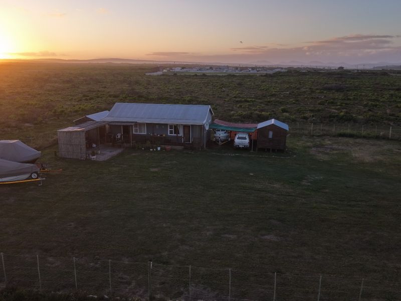 Aerial view of a rural property featuring a modest dwelling with a corrugated metal roof set within a large, fenced plot at sunset.