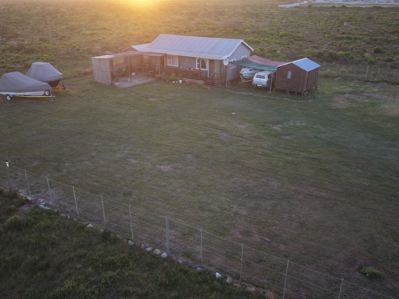 Aerial view of a detached house with a corrugated metal roof, set on a large plot of land with perimeter fencing and an outbuilding.