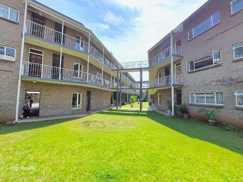 A view of the apartment complex courtyard featuring brick facades, elevated walkways connecting the buildings, and a central lawn area.