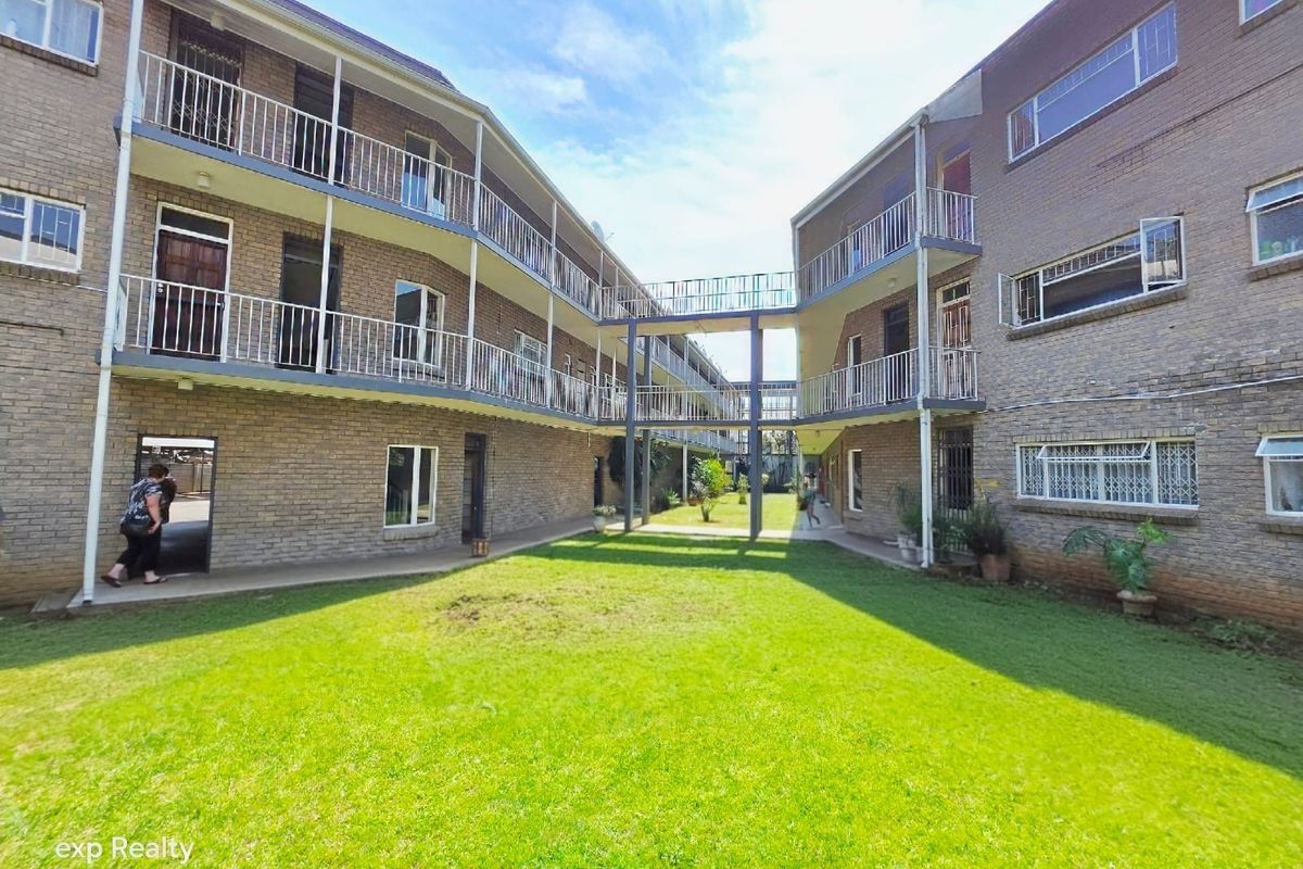 A view of the apartment complex courtyard featuring brick facades, elevated walkways connecting the buildings, and a central lawn area.