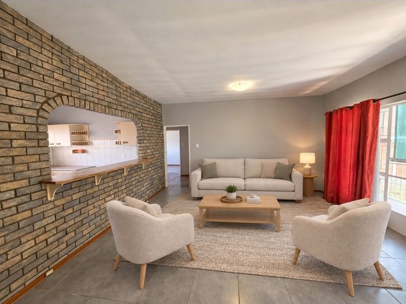 Open plan living area featuring a distinctive exposed brick wall with a breakfast bar opening into the kitchen and neutral tiled flooring.