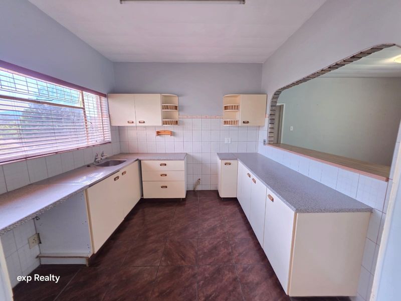 A dated kitchen featuring built-in cabinetry, laminate countertops, and tiled finishes, offering a functional layout ready for modernization.