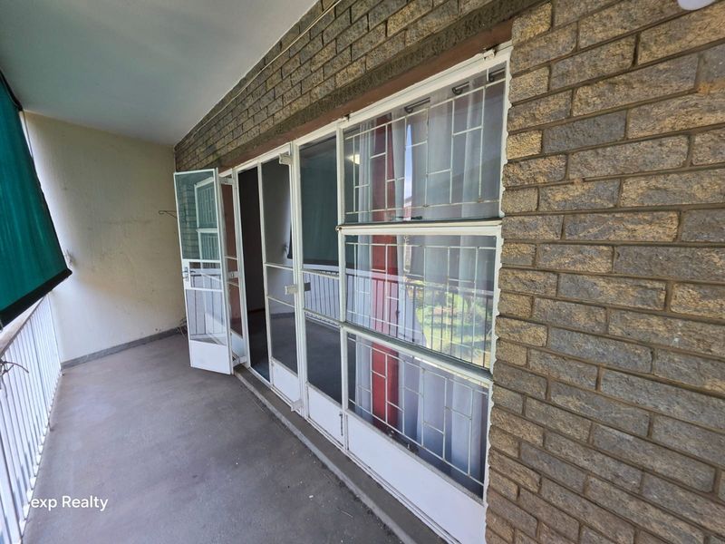 A covered balcony featuring a brick facade, concrete flooring, and metal security gates providing access to the interior.