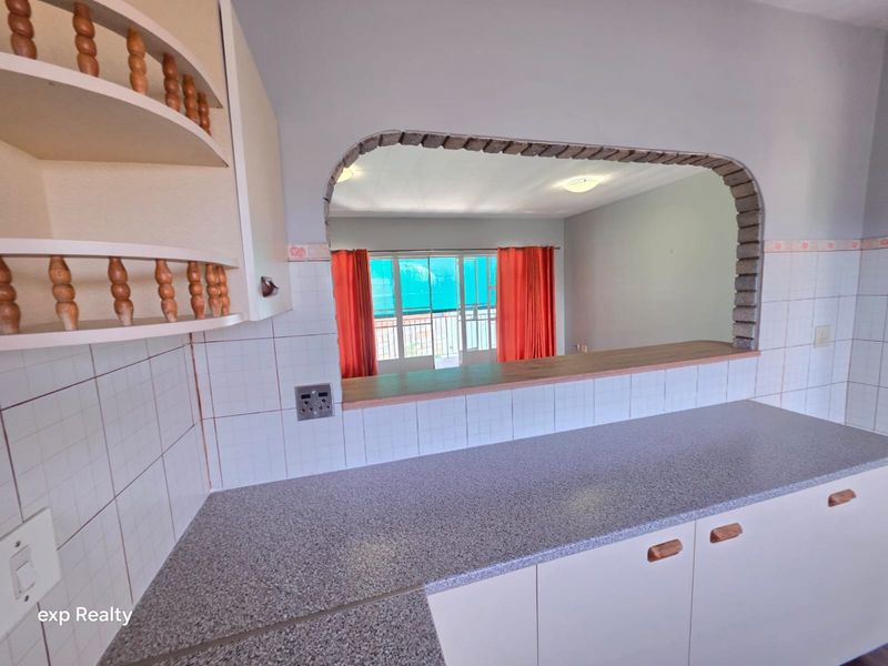 A functional kitchen featuring laminate countertops, tiled splashbacks, and a convenient pass-through window overlooking the living area.