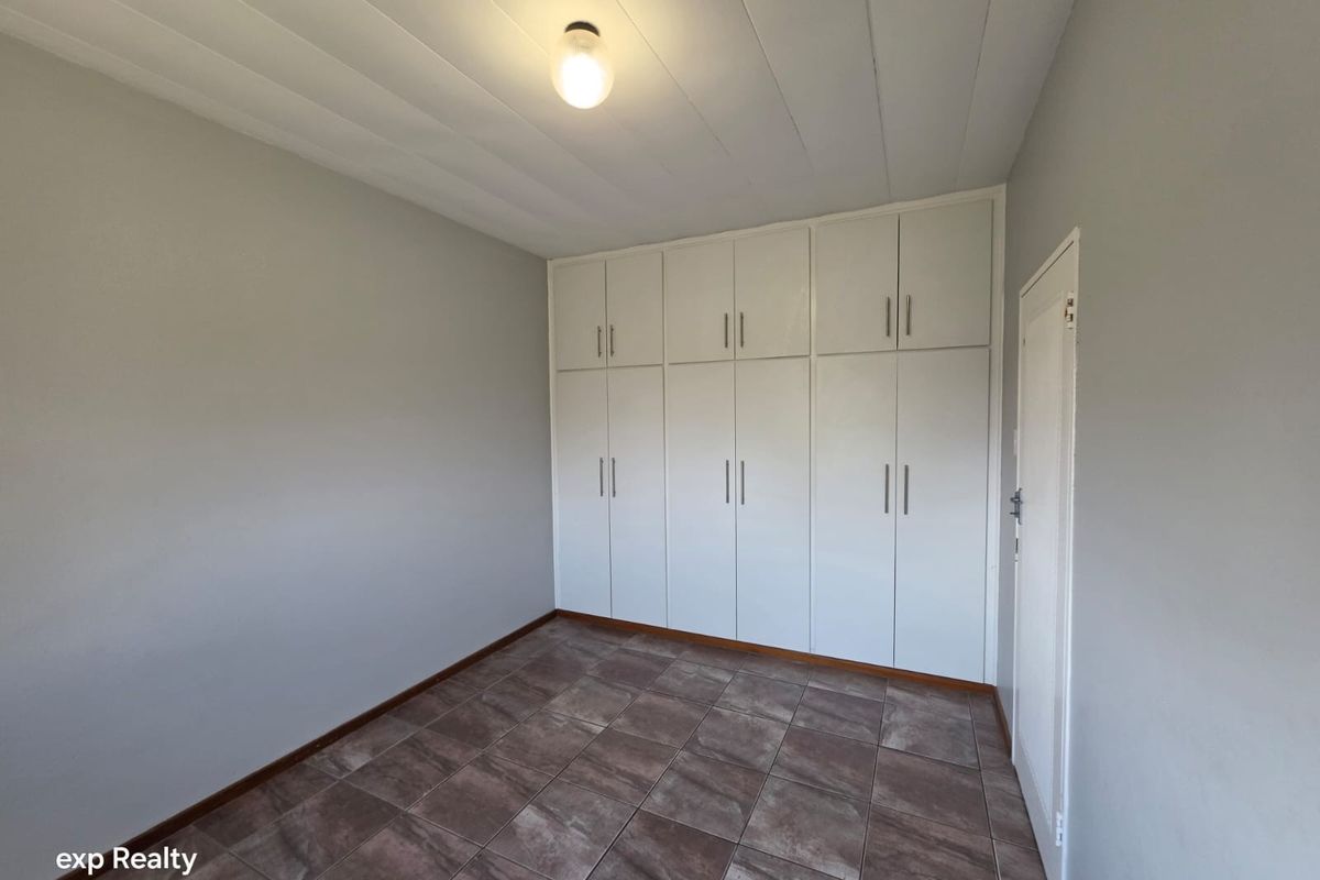 A clean, empty bedroom featuring neutral grey walls, tiled flooring, and extensive white built-in cupboards for ample storage.