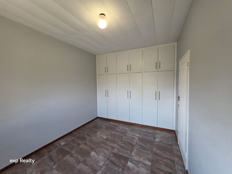 A clean, empty bedroom featuring neutral grey walls, tiled flooring, and extensive white built-in cupboards for ample storage.