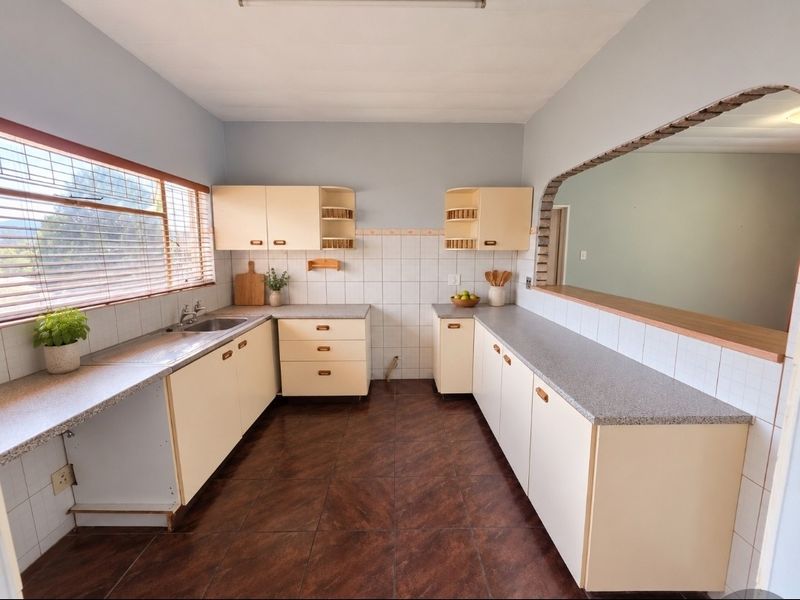 A functional kitchen featuring dated cabinetry, laminate countertops, tiled backsplash, and an open archway connecting to the adjacent living space.