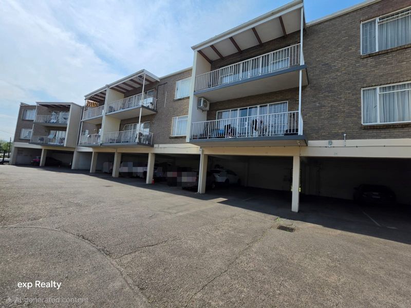 Exterior view of a multi-story apartment building featuring brick facade, private balconies with metal railings, and ground-level covered parking spaces.