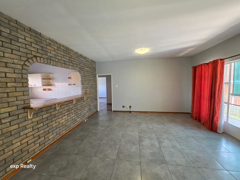 Spacious living area featuring a brick accent wall with a pass-through to the kitchen, tiled flooring, and access to an outdoor balcony.