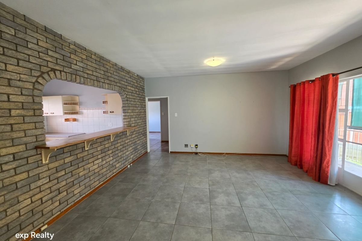 Spacious living area featuring a brick accent wall with a pass-through to the kitchen, tiled flooring, and access to an outdoor balcony.