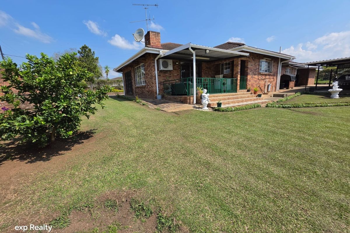 Rear view of a brick-faced small holding residence featuring a covered patio, established garden, and exterior security fixtures.