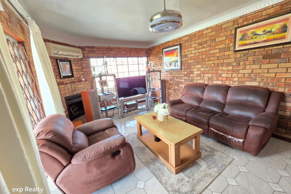 A living room featuring exposed brick walls, tiled flooring, a ceiling fan, and a built-in fireplace, providing a rustic and cozy atmosphere.
