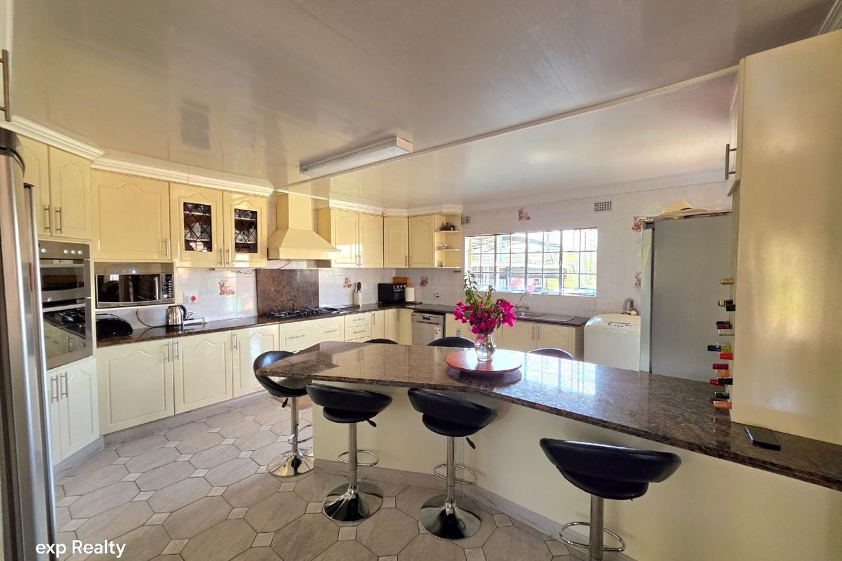 Spacious kitchen featuring cream cabinetry, granite countertops, a central island with breakfast bar seating, and integrated appliances.
