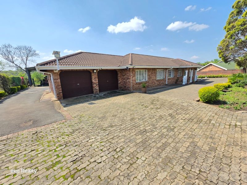 Front exterior view of a brick-faced small holding property featuring a double garage, tiled roof, and extensive paved driveway area.