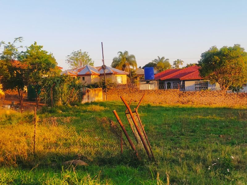A view of a vacant residential plot featuring a perimeter wall with razor wire and a water storage tank in a suburban setting.