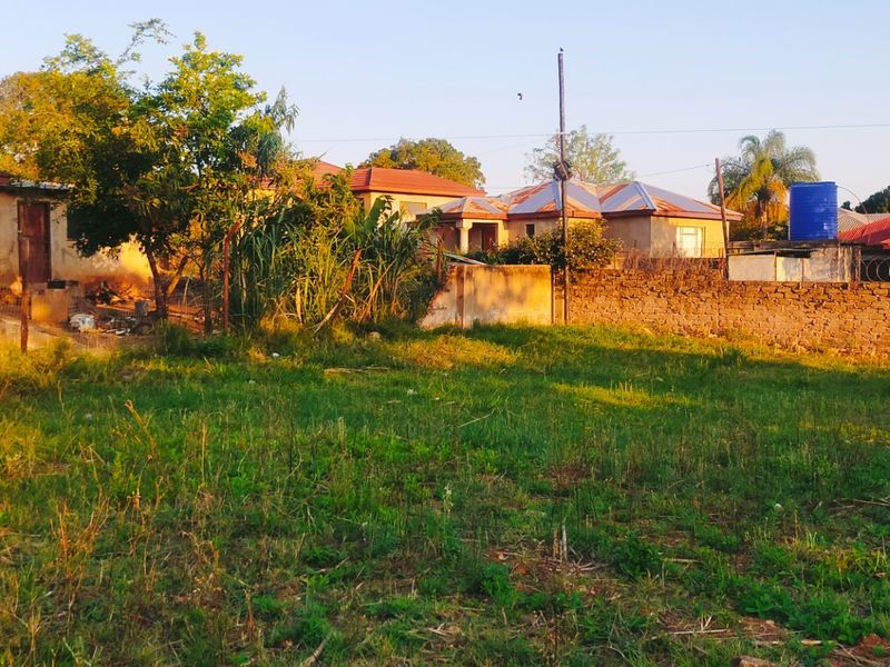 A view of a vacant residential plot featuring a brick boundary wall with security razor wire and an existing water storage tank.