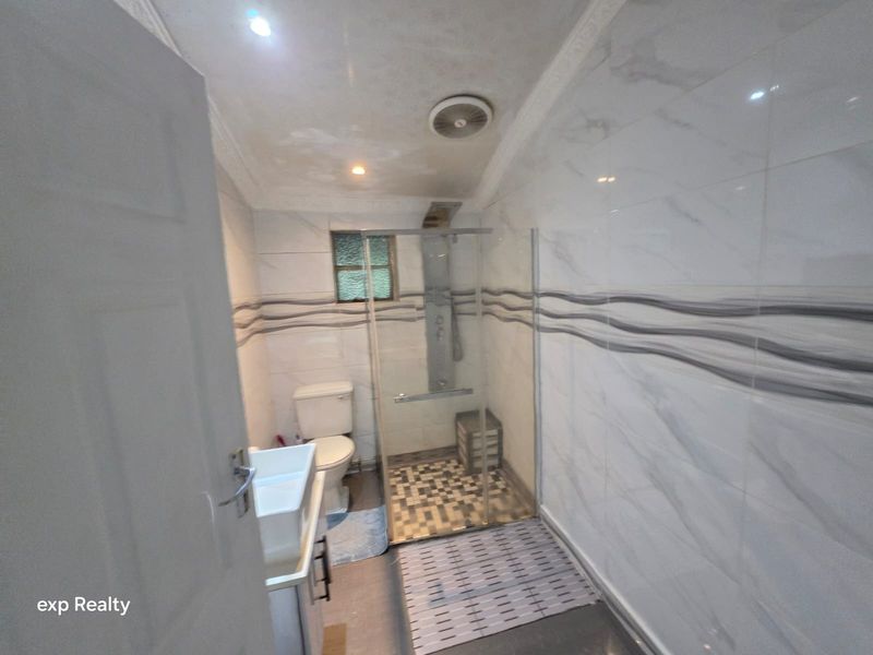 A modern bathroom featuring a glass shower enclosure, toilet, and vanity basin with contemporary wall tiling and an extractor fan.