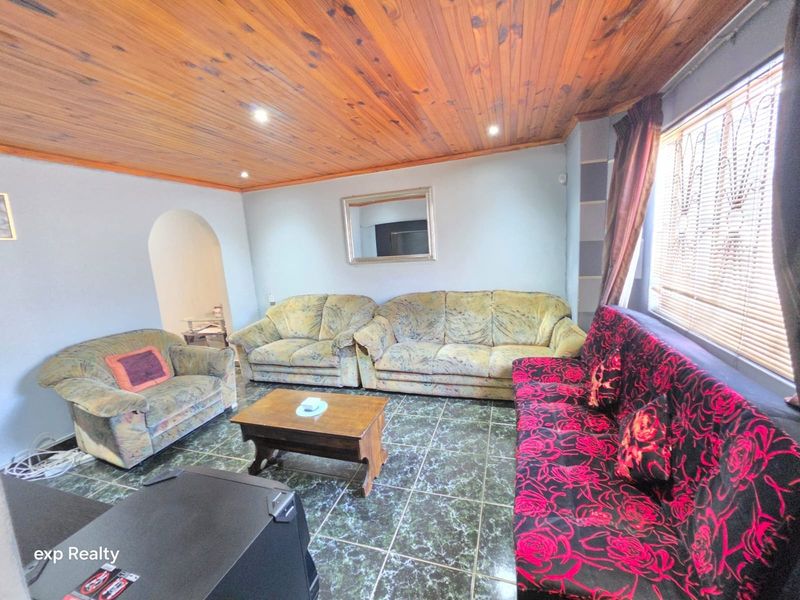 A living room featuring a timber tongue and groove ceiling, ceramic tiled flooring, and an arched entryway leading to adjacent spaces.