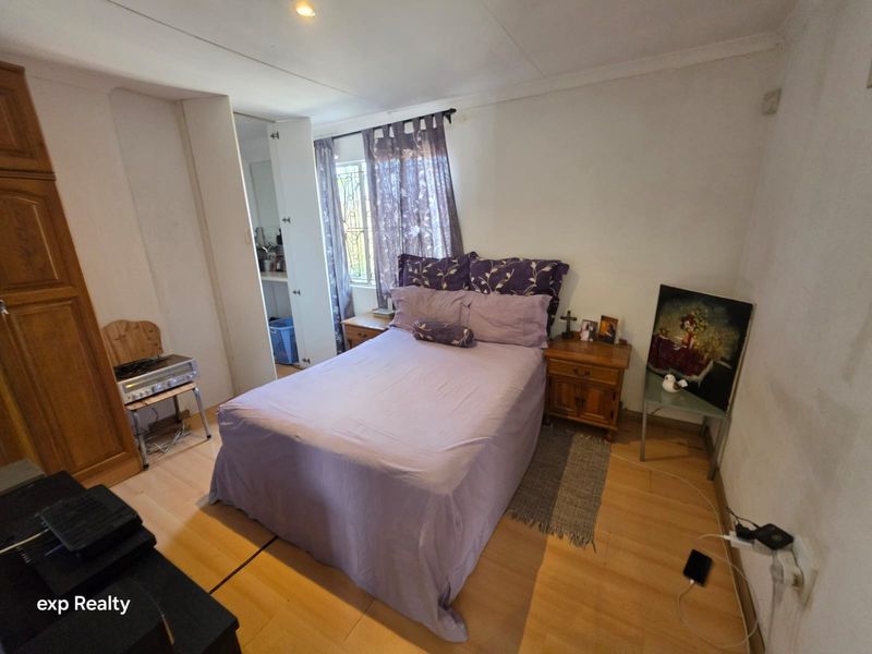 A functional bedroom featuring laminate flooring, built-in cupboards, and security bars on the window, offering a practical space for rest.