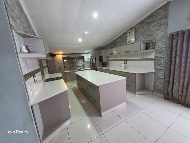 Modern kitchen featuring a central island, stone countertops, built-in cabinetry, and a stone veneer feature wall with tiled flooring and recessed lighting.