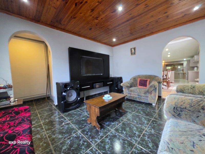 A living room featuring a timber tongue and groove ceiling, tiled flooring, and arched doorways leading to adjacent living spaces.