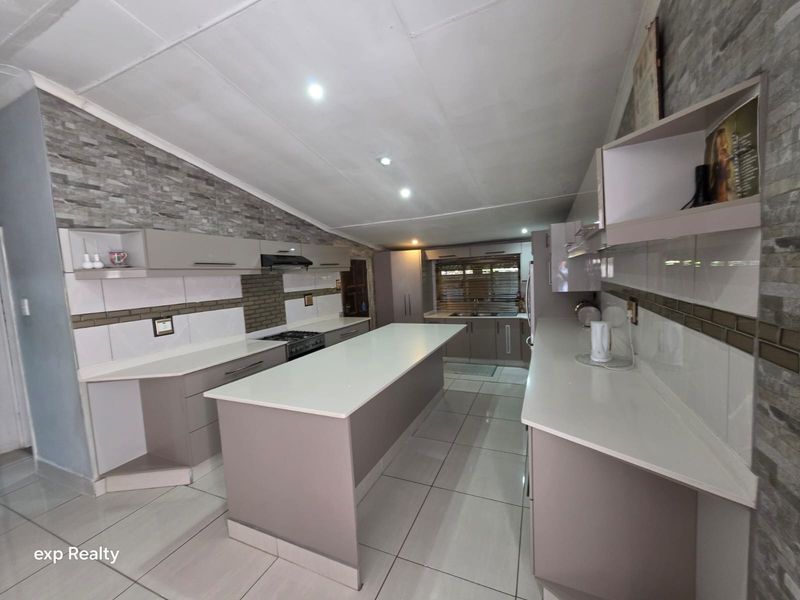 Modern kitchen featuring a central island, stone countertops, ample built-in cabinetry, and a stylish stone veneer feature wall with recessed lighting.