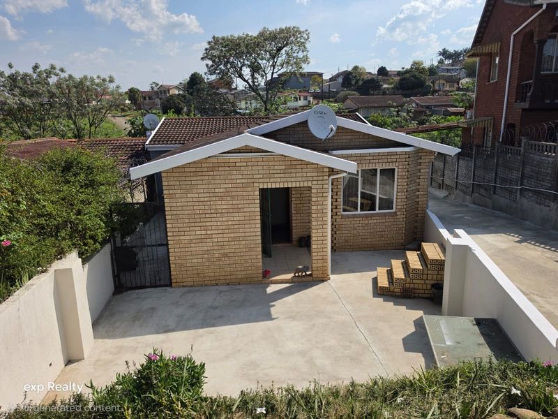 Front view of a face brick house featuring a concrete driveway, tiled roof, and boundary wall in a residential neighborhood.