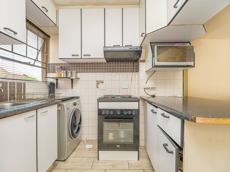 A compact kitchen featuring white cabinetry, dark laminate countertops, tiled backsplash, and a freestanding stove with an extractor fan.