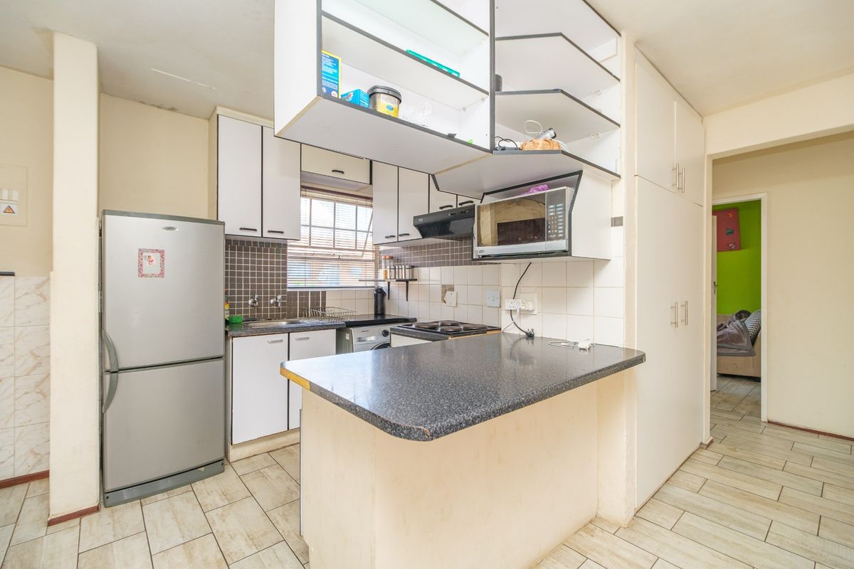 Compact kitchen featuring built-in cabinetry, a breakfast bar, tiled backsplash, and integrated appliances, offering a functional layout with potential for modern updates.