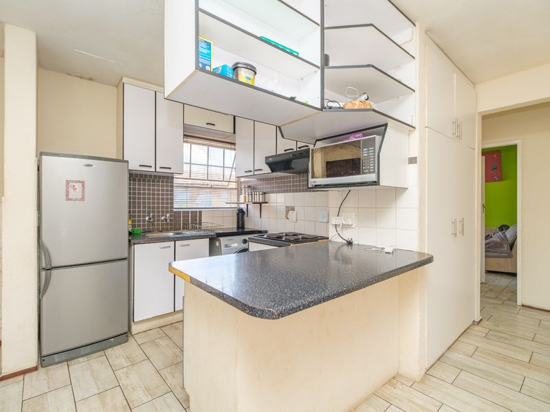 Compact kitchen featuring built-in cabinetry, a breakfast bar, tiled backsplash, and integrated appliances, offering a functional layout with potential for modern updates.