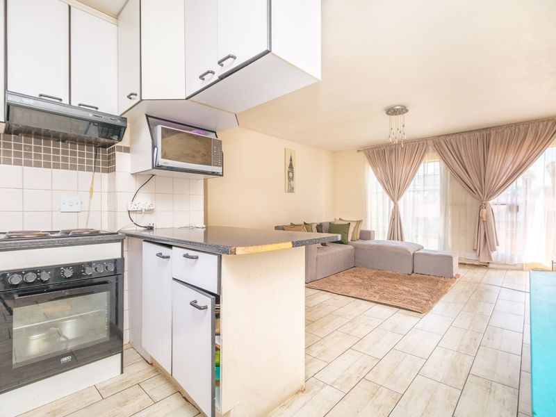 Open-plan living area featuring a functional kitchen with built-in oven and hob, flowing into a bright lounge space with access to a balcony.