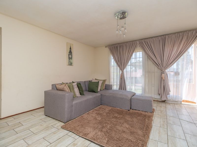 A bright living room featuring light-toned tiled flooring and a large sliding glass door that provides access to the outdoor area.