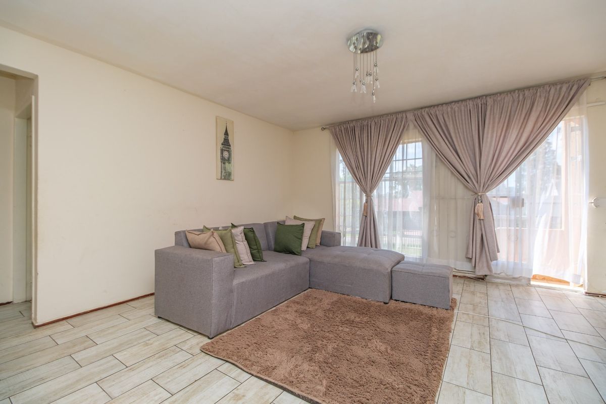 A bright living room featuring light-toned tiled flooring and a large sliding glass door that provides access to the outdoor area.