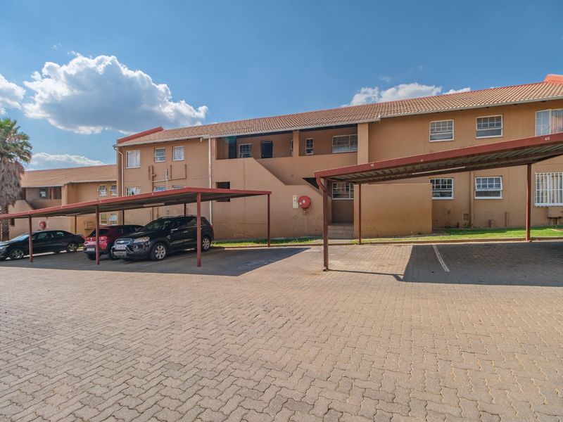 Exterior view of an apartment complex featuring a paved parking area with covered carports and multi-story residential units.