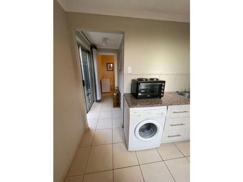 A functional laundry area featuring tiled flooring, granite countertops, and built-in cabinetry, with direct access to an adjacent room through a sliding glass door.
