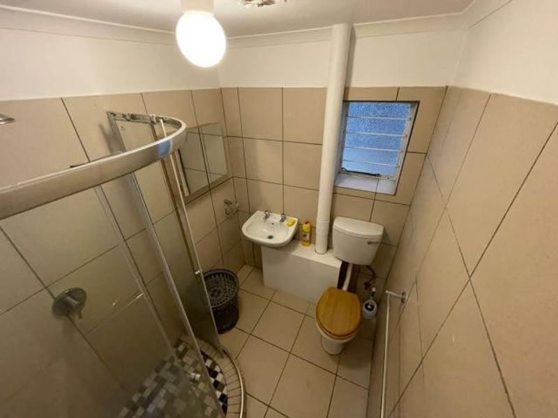 Compact bathroom featuring a curved glass shower enclosure, wall-mounted basin, and toilet with neutral wall and floor tiling.