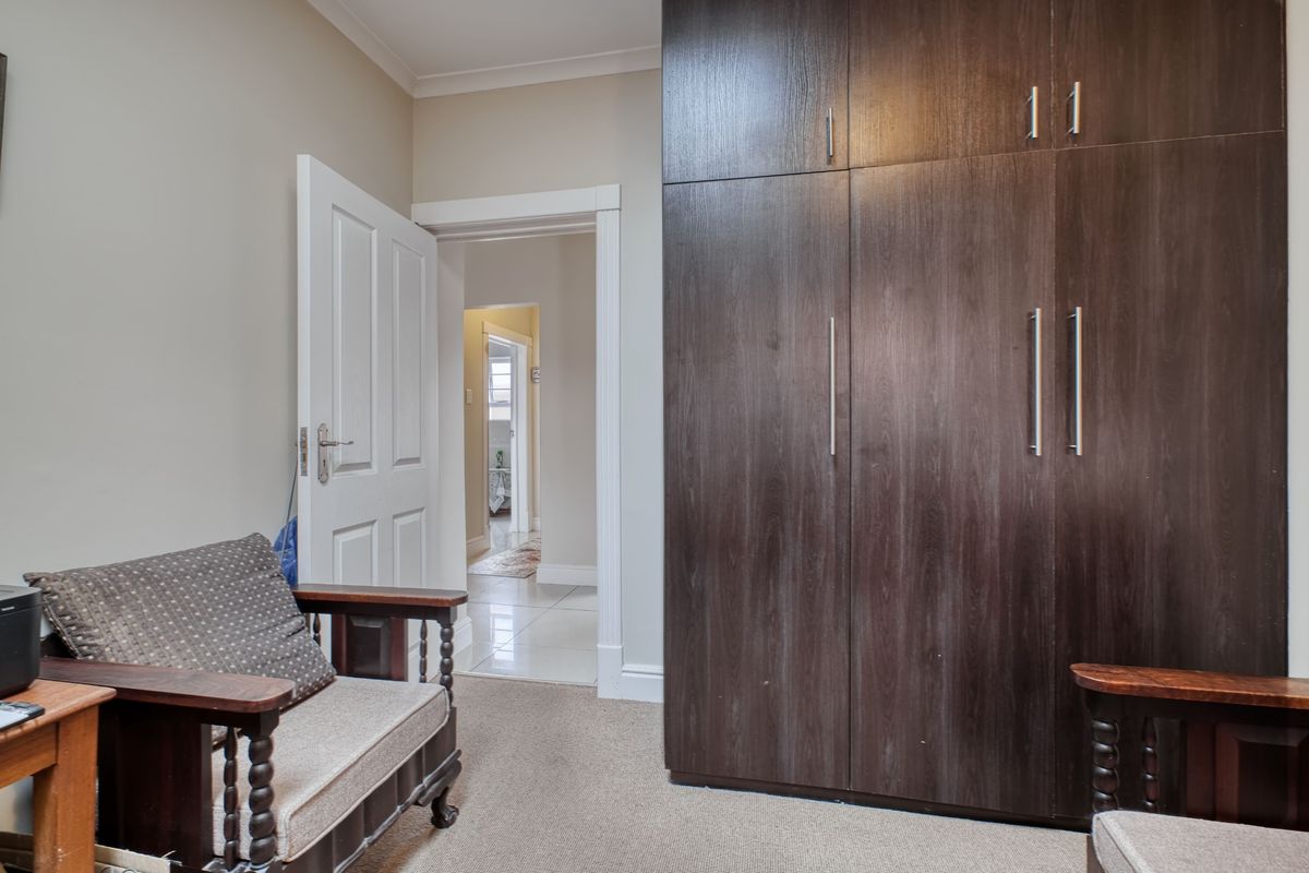 A bedroom featuring dark wood built-in cupboards, neutral wall finishes, and carpeted flooring, with a view through to the hallway.