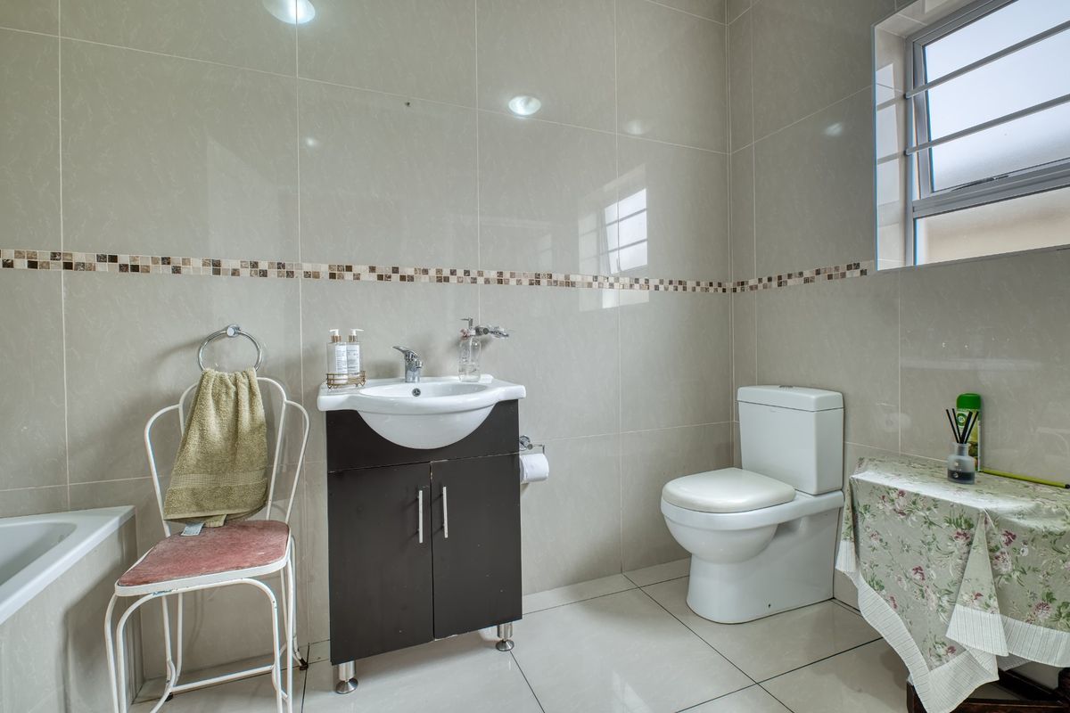 A well-maintained bathroom featuring tiled walls and flooring, a vanity unit with a washbasin, a toilet, and a bathtub.
