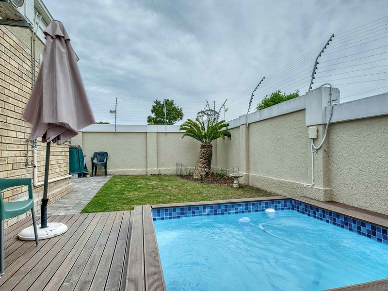 A private outdoor pool area featuring timber decking, a small lawn, and secure perimeter walls with electric fencing.